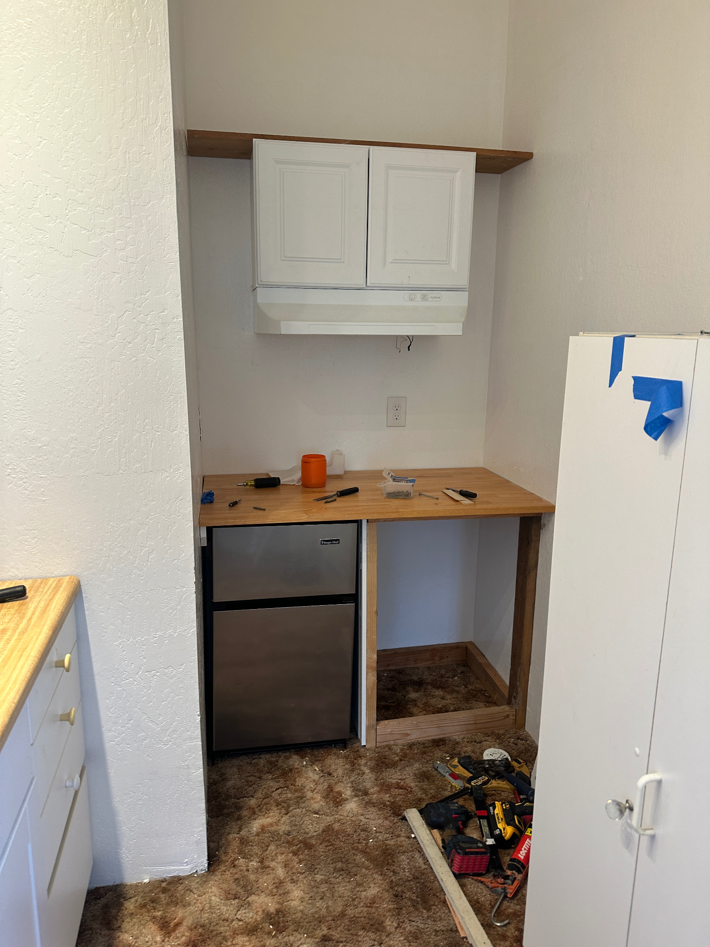 Kitchenette before remodel — dated cabinets, worn carpet, and demo in progress